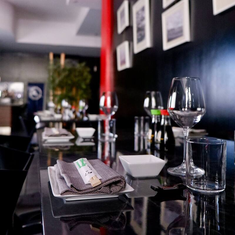 foto del tavolo apparecchiato con calici di vino, bicchieri, tovagliolo in cotone, bacchette in lego per sushi, porta bacchette di colore nero e ciottolina in ceramica bianca per soia