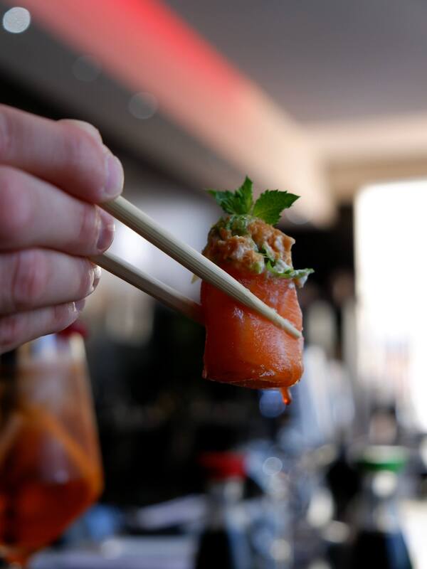 primo piano di bachette sushi che tengono gunkan spice sake, sfera di riso avvolta da salmone con sopra tartare di salmone piccante